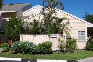 A photo of the home at 200 Champions Way, with peach paint, a fence covering some palm trees and two parking spaces.